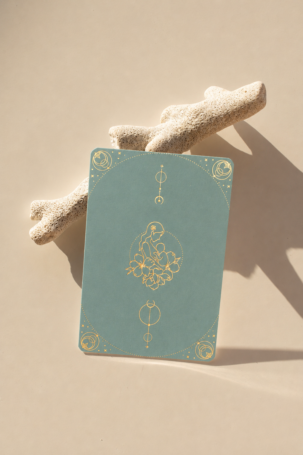 Blissful Birth affirmation card in dusty blue with gold foil mother-and-baby illustration, resting on coral.